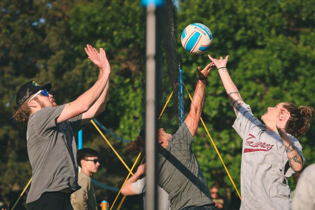 Co-Ed volleyball players jumping to spike a ball at the net in an outdoor league.