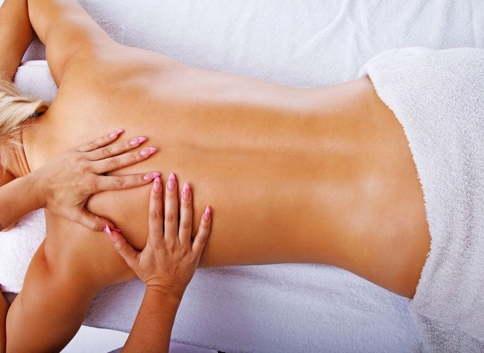 Un'estetista applica uno scrub esfoliante sulla coscia di una persona sdraiata su un lettino bianco.