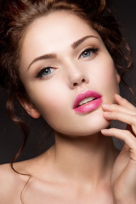 Ritratto ravvicinato di una donna con il rossetto rosa, che tiene la mano vicino al mento.