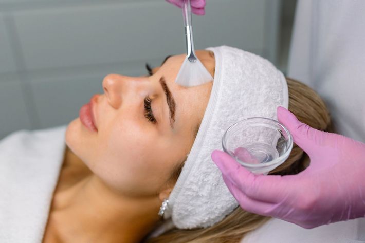 Trattamento cosmetico sul viso di una donna con mani guantate e applicatore di gel.