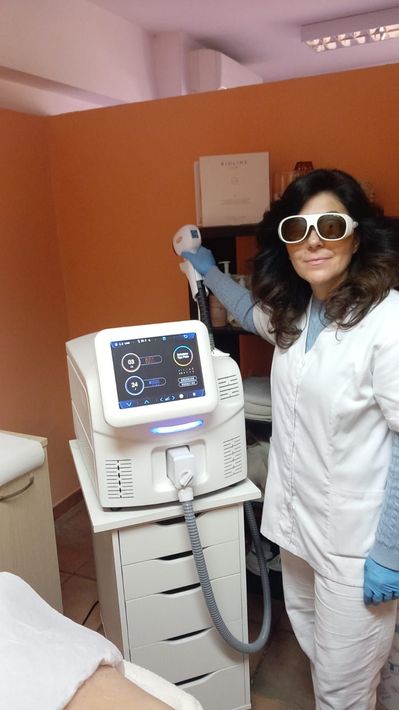 Una persona con camice bianco e occhiali da sole è in piedi accanto a un macchinario medico in una stanza di una clinica.