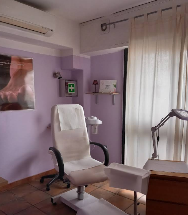 Sala visite mediche color lavanda con sedia bianca e lampada per trattamenti sopra la finestra.