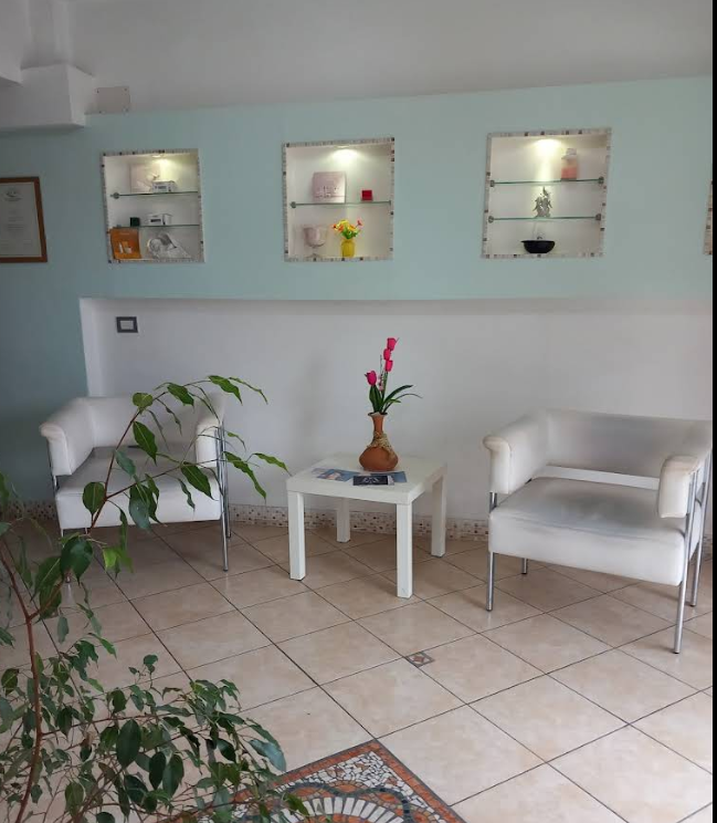 Luminosa sala d'attesa con due sedie bianche, un tavolino, piante in vaso e mensole a muro.