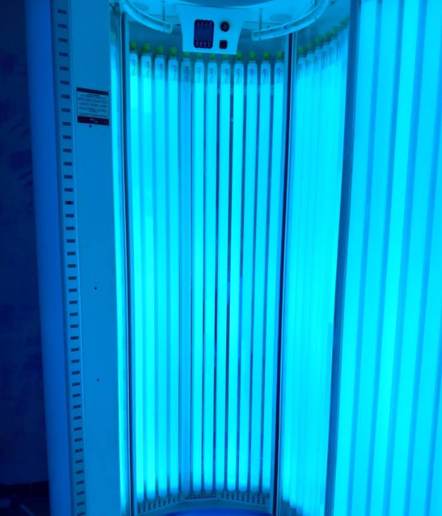 Cabina abbronzante illuminata di blu con tubi luminosi verticali e pannello di controllo in alto.