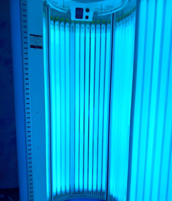 Cabina abbronzante illuminata di blu con tubi luminosi verticali e pannello di controllo in alto.