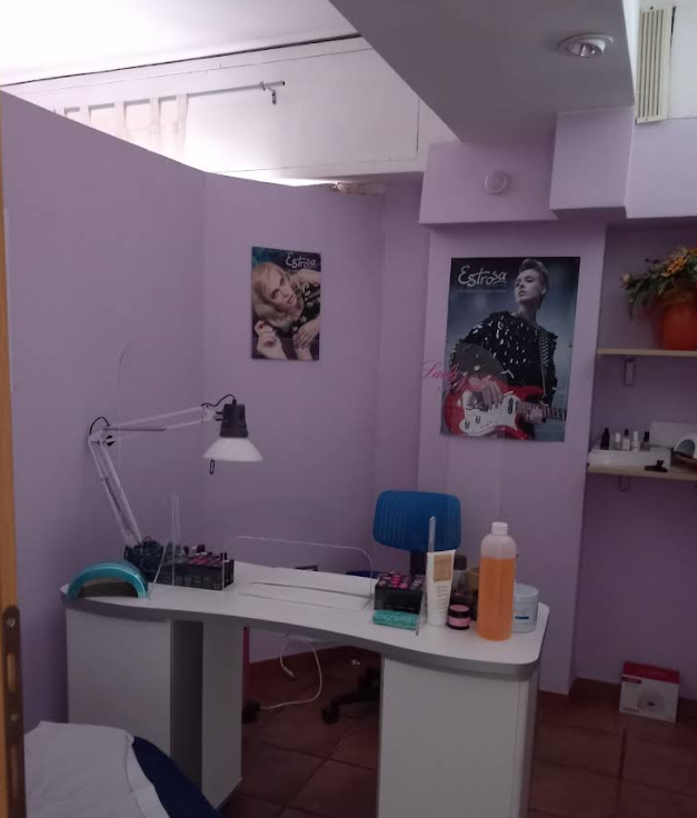 Scrivania da salone di bellezza color lavanda con lampada, sedia, flaconi di smalto e poster alle pareti.