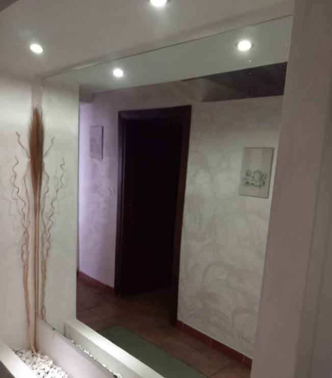 Corridoio rivestito di specchi con faretti a incasso, pareti beige e una porta scura in fondo.