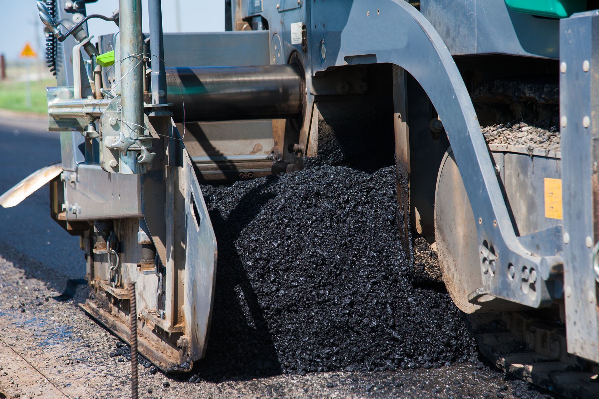 Asphalt paving machine laying black asphalt on a road surface.