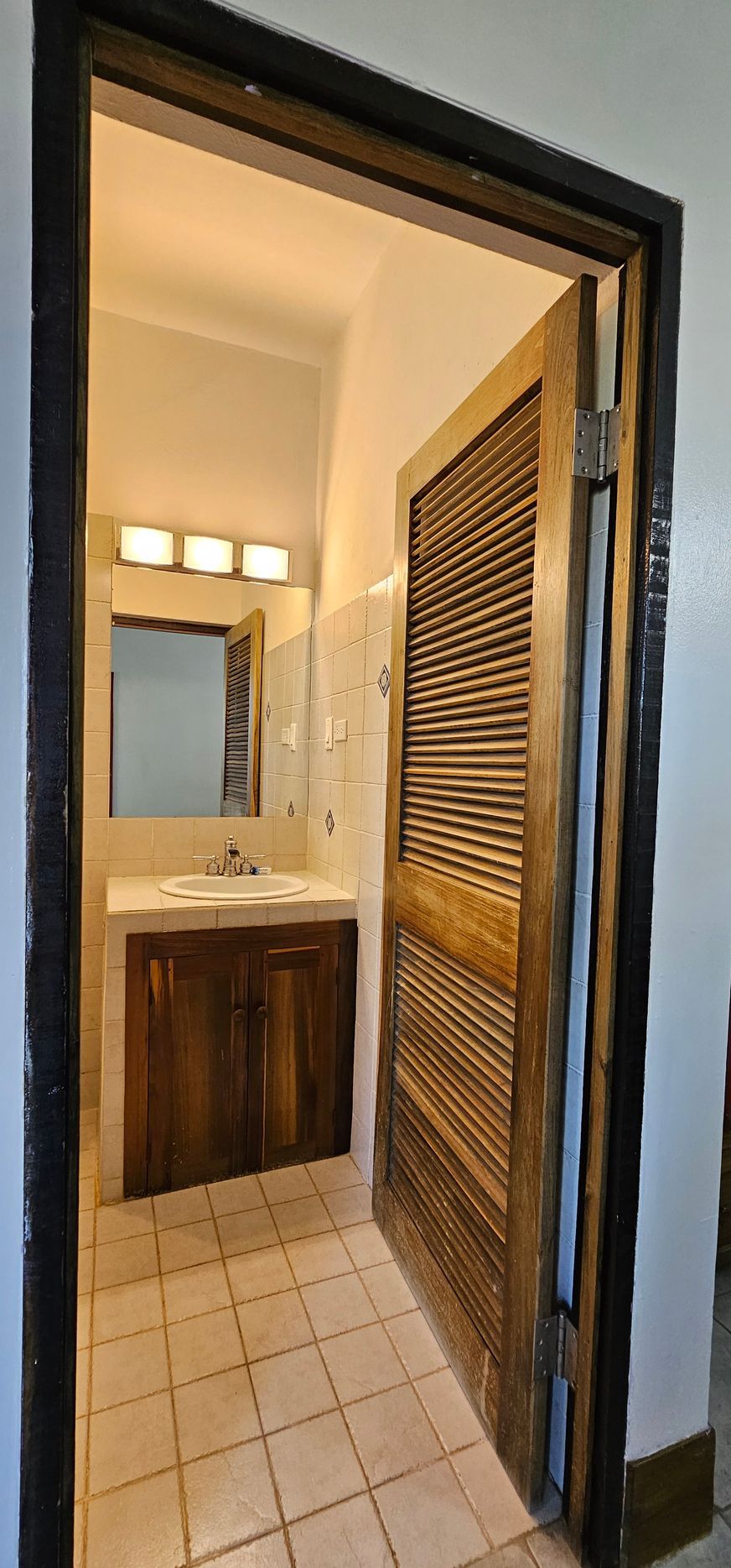 Open bathroom door revealing a vanity with mirror and lights, and tiled floor.