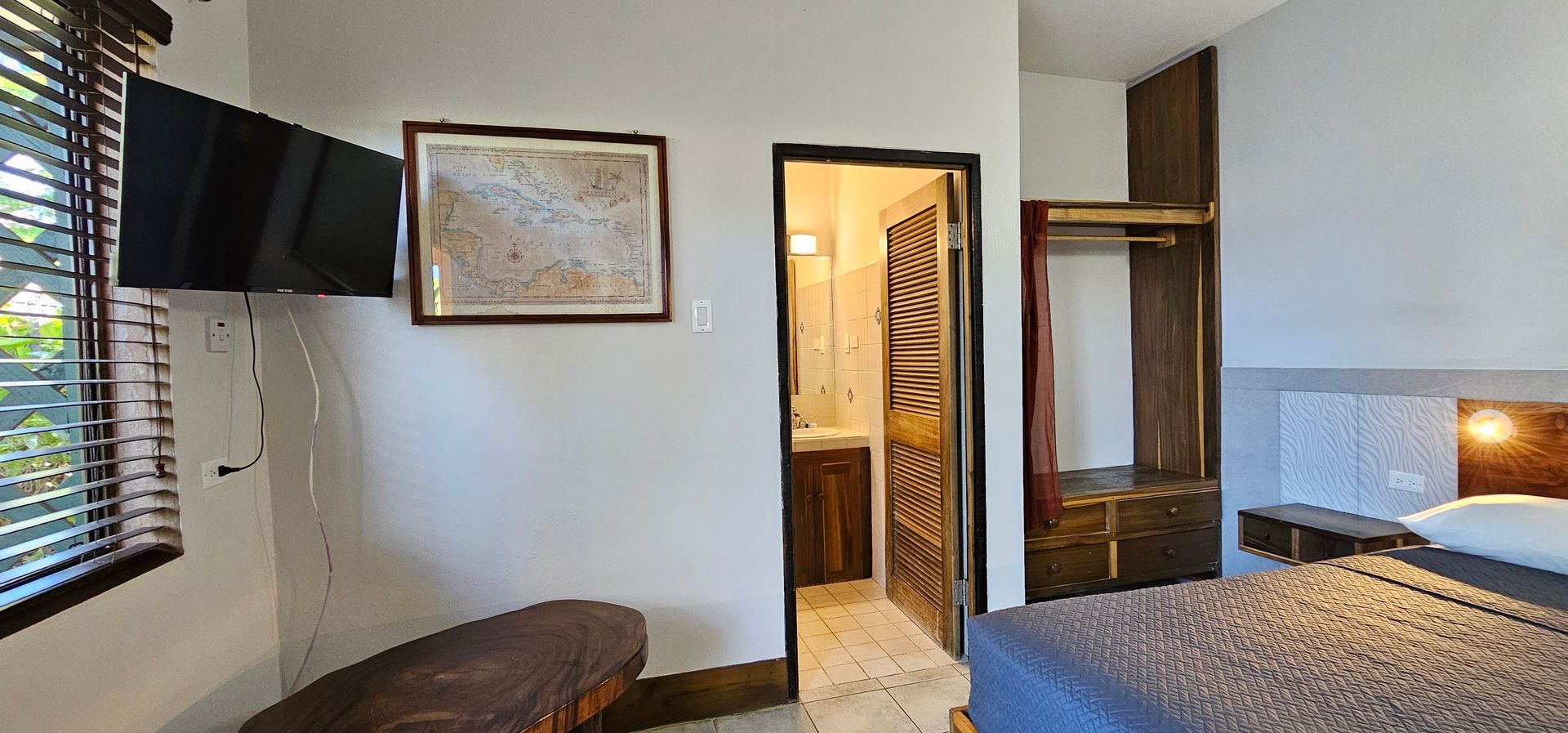 A room with a bed, a TV, a wooden bench, and a bathroom door.