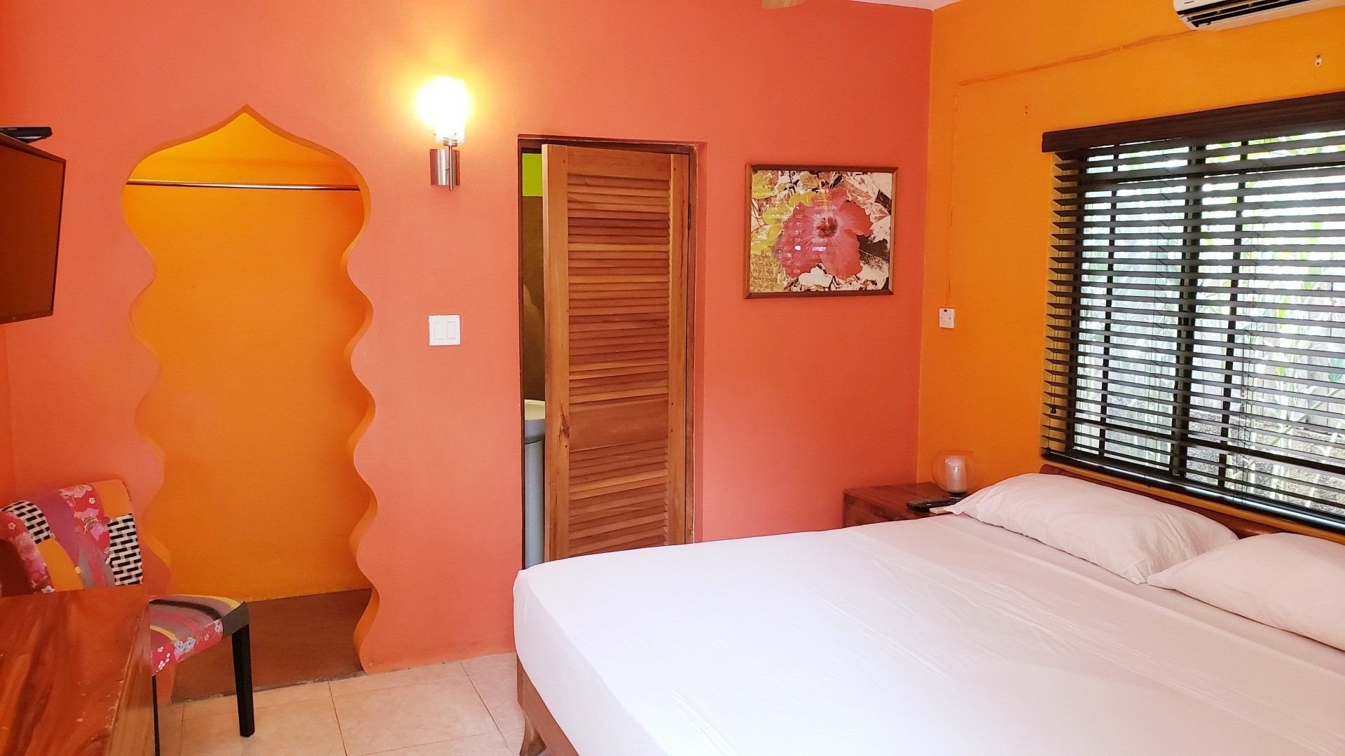 A bedroom with a bed , chair , window and orange walls.