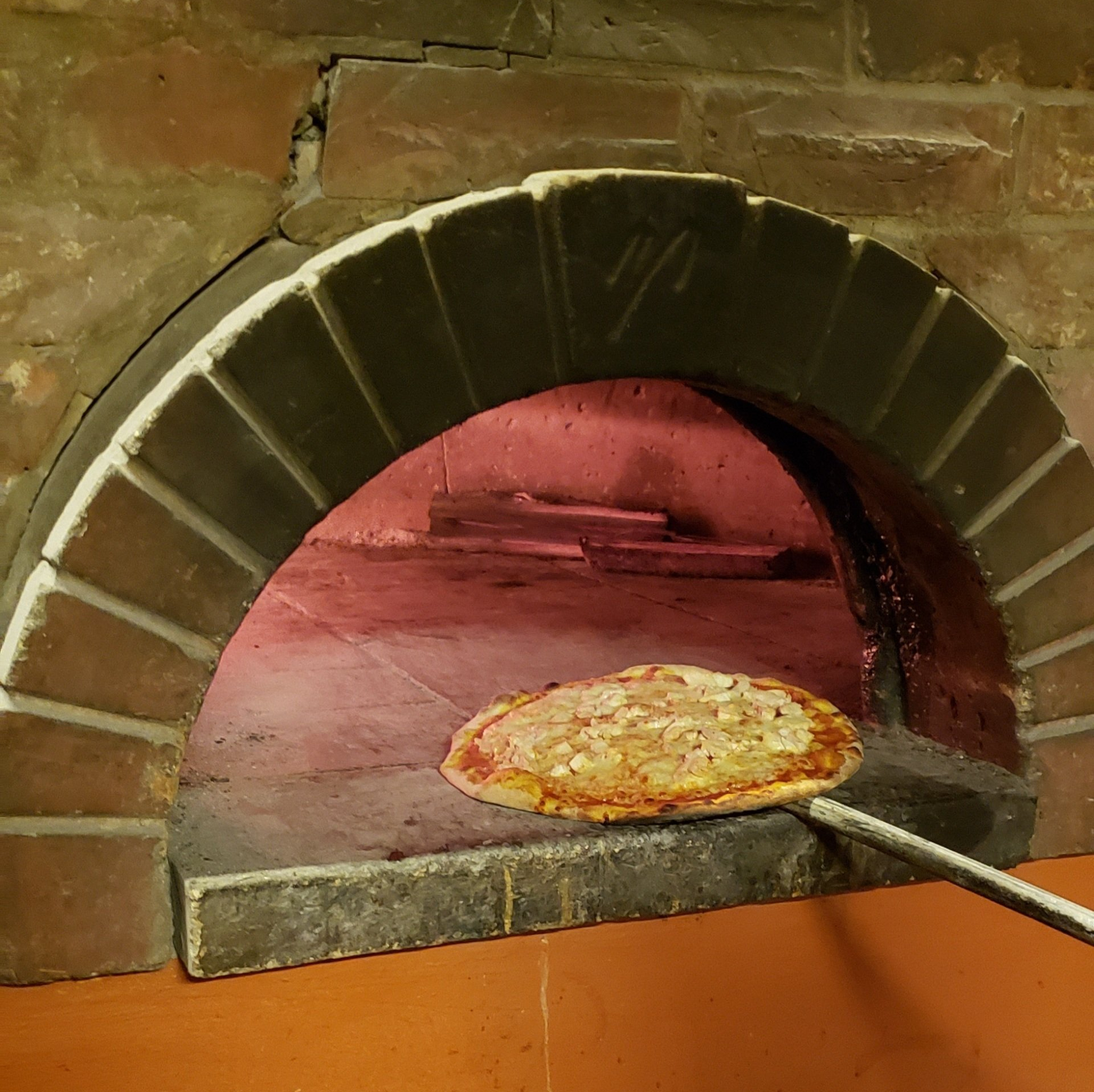 A pizza is being taken out of a brick oven
