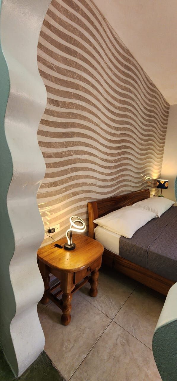 A bedroom with a bed , nightstand , lamp and striped wall.