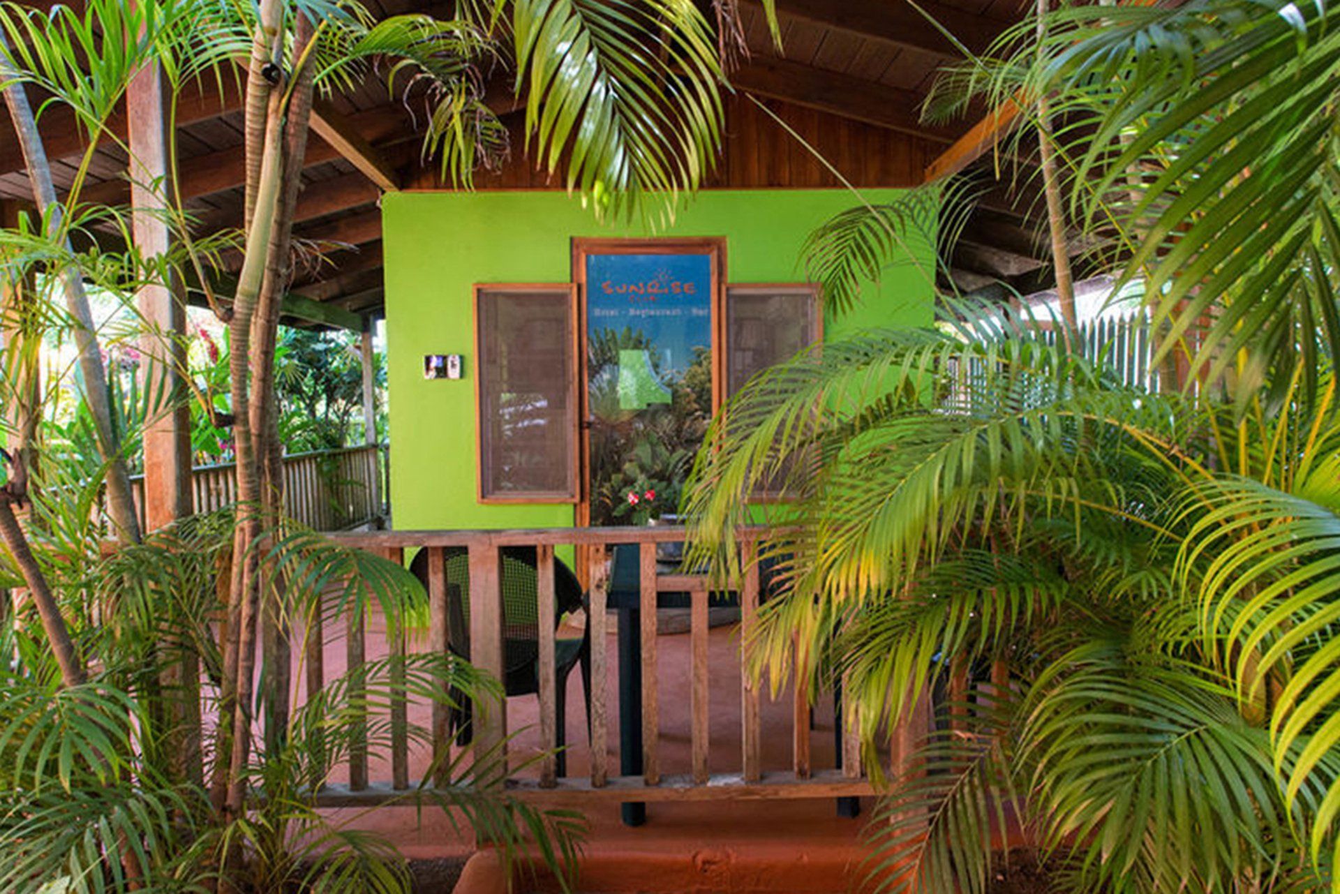 A green house with a balcony surrounded by palm trees
