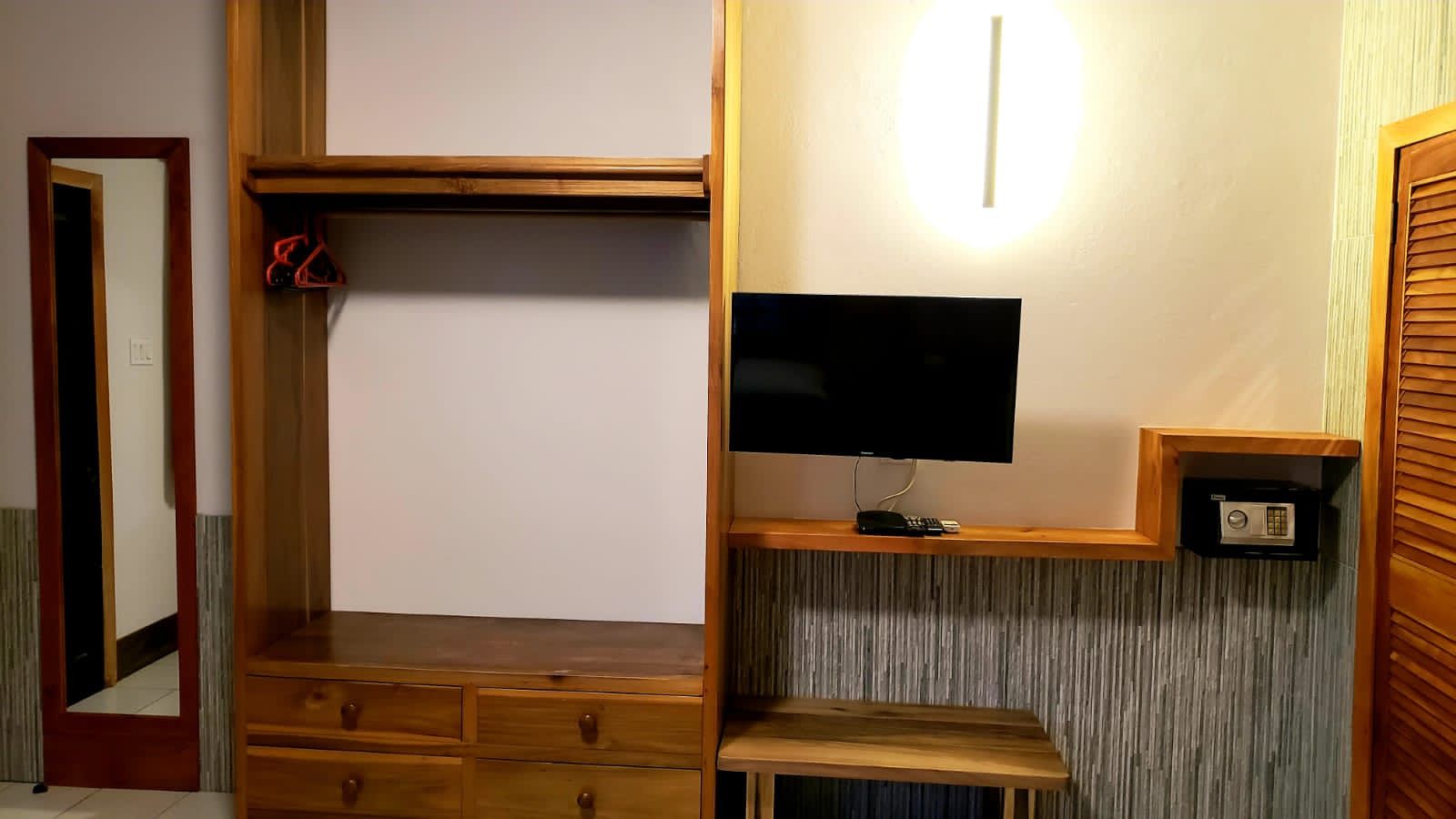 A hotel room with a desk , dresser , television and mirror.