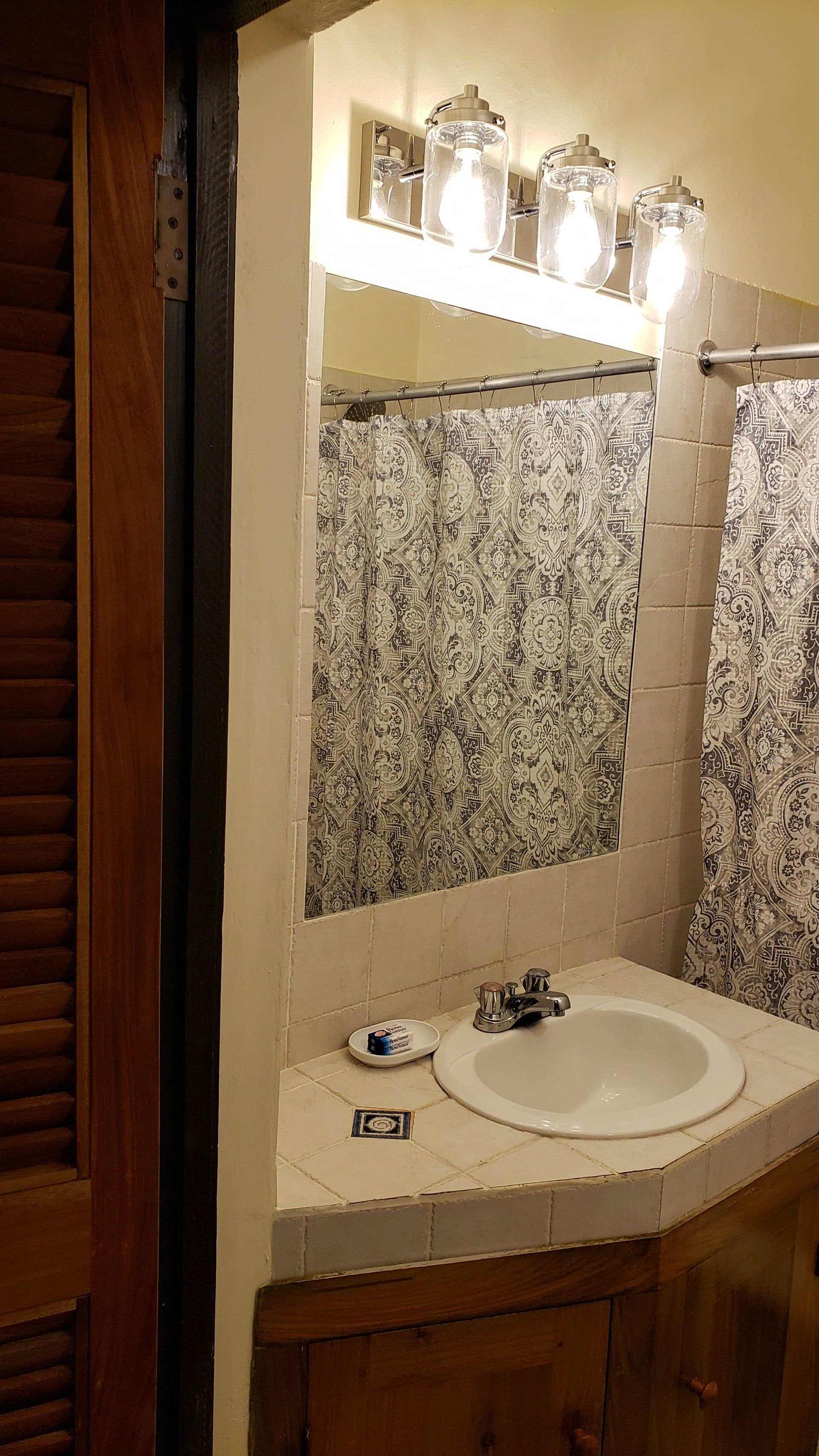 A bathroom with a sink , mirror and shower curtain.