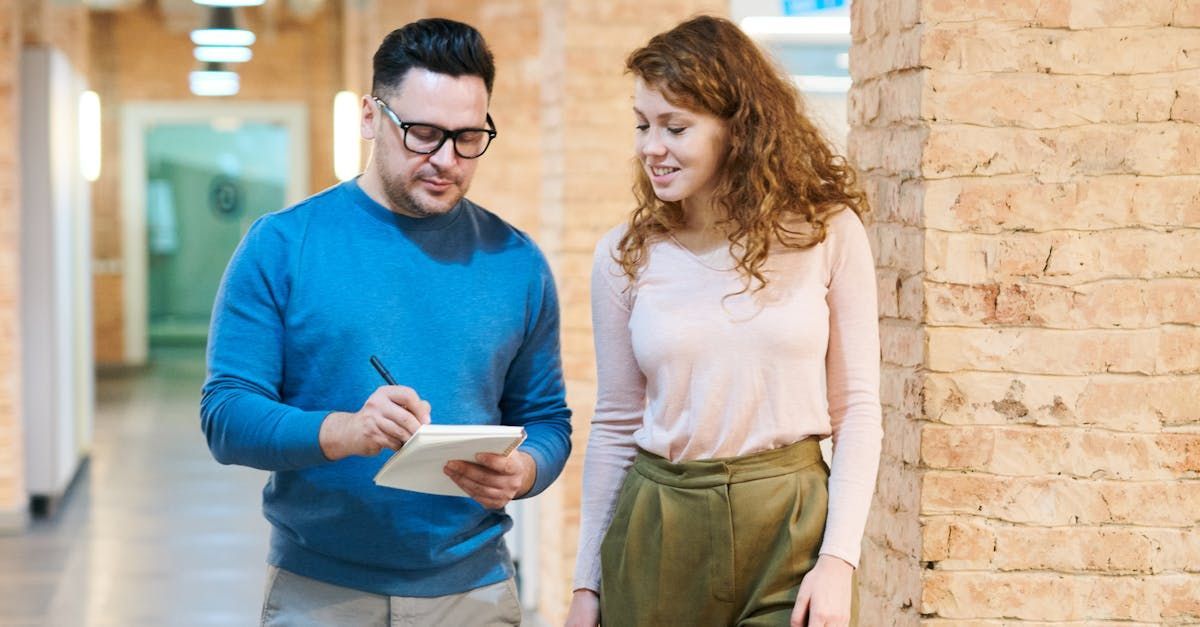 A man and a woman are standing next to each other in a hallway looking at a tablet.