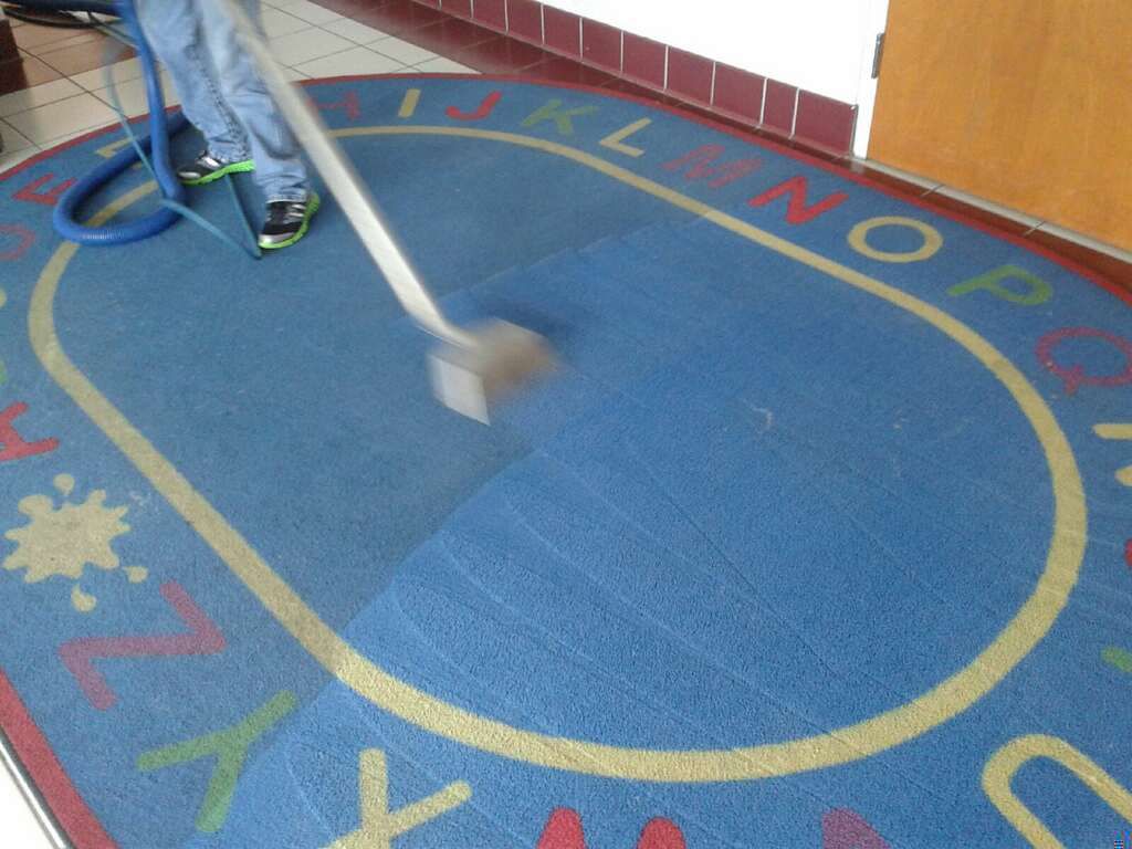 Child mopping a blue classroom rug with a yellow border and colorful alphabet letters