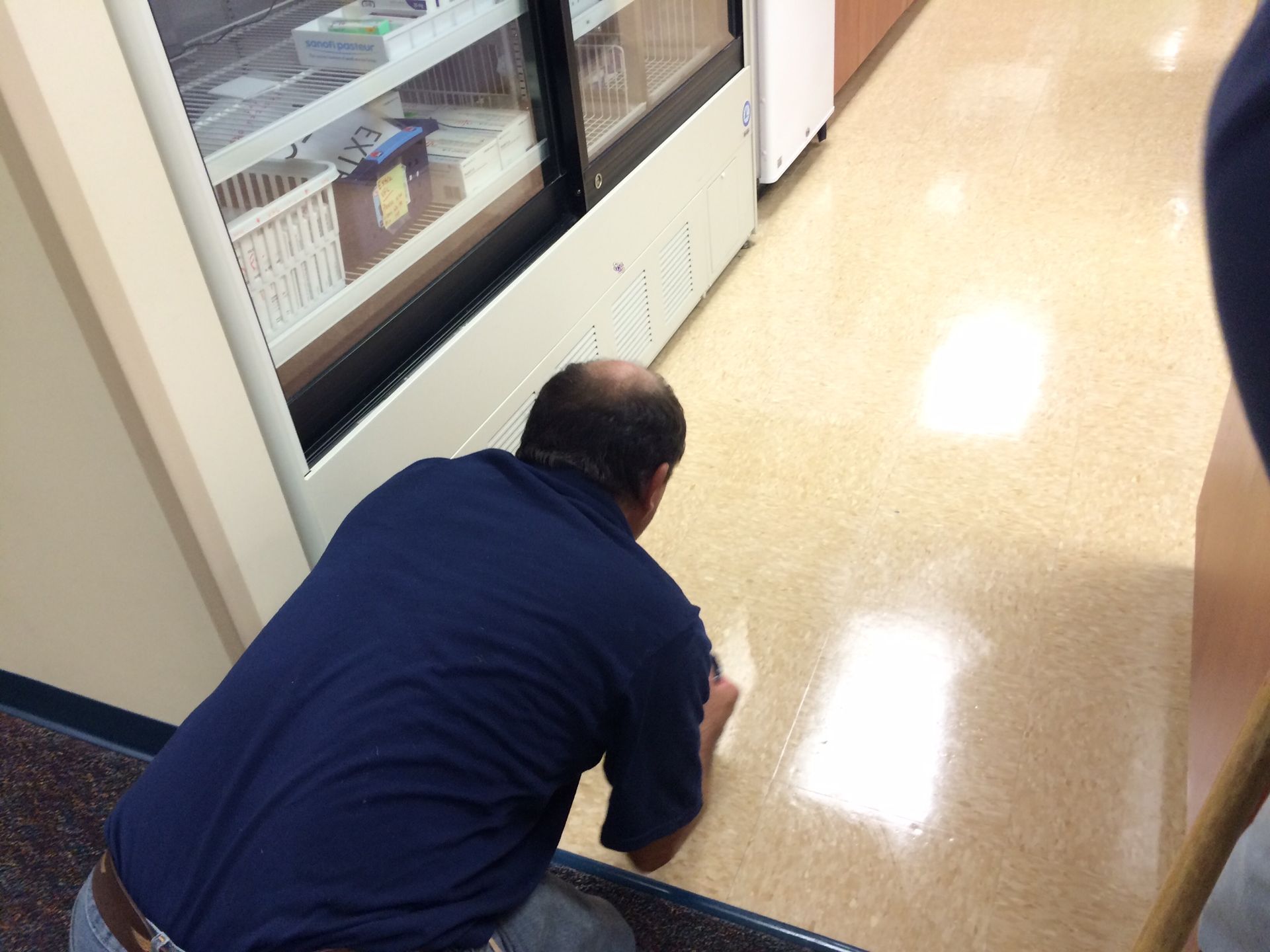 Person in a blue shirt crawling on a hallway floor beside glass display cases.