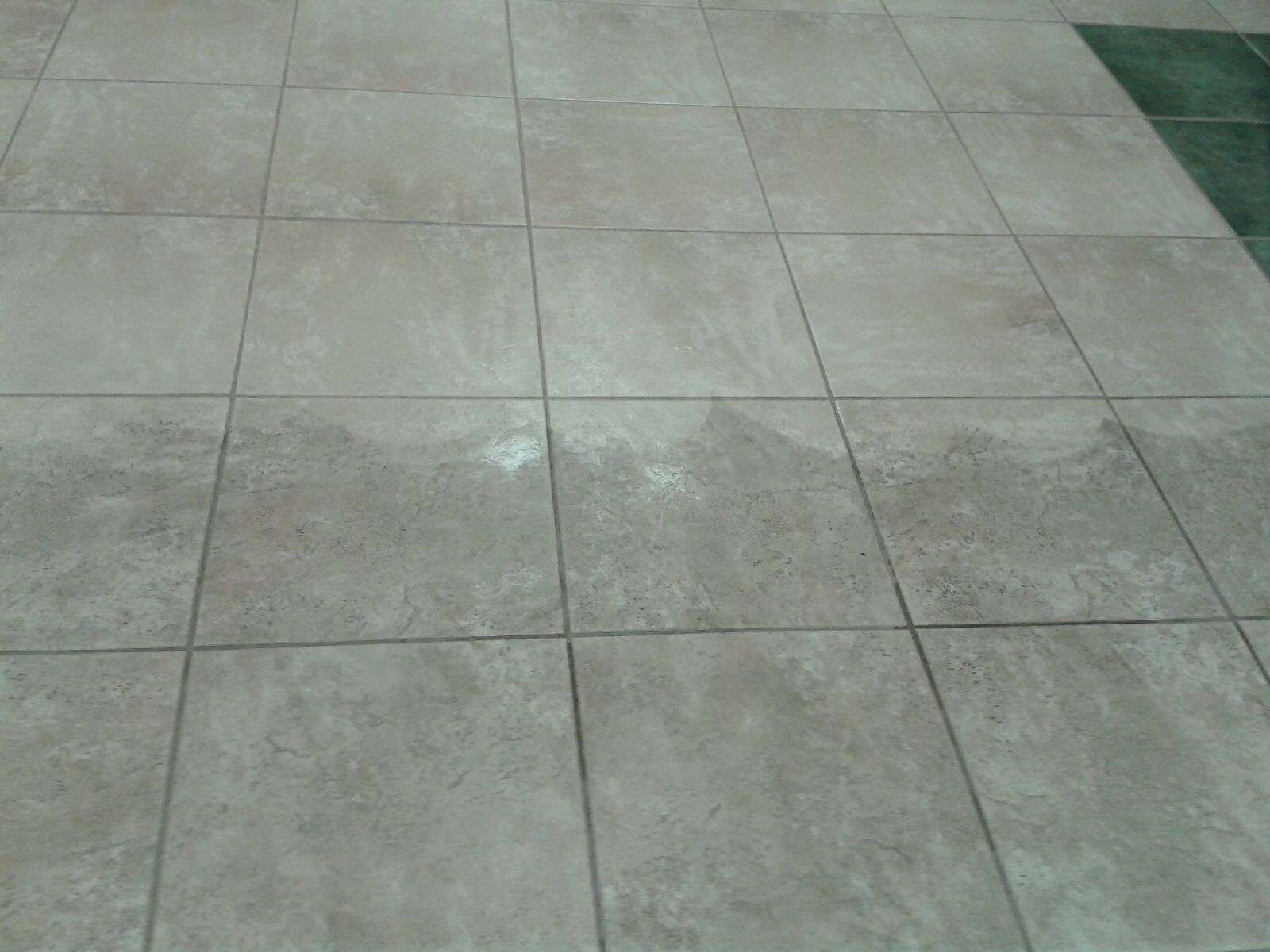 Gray tiled floor with a few white scuff marks and a green edge at the top right.