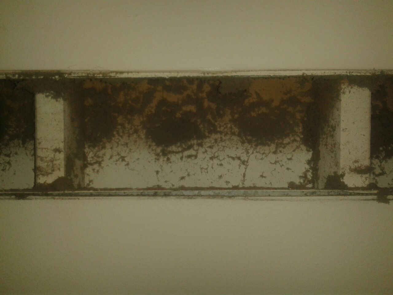 Rusty metal beam on a white wall, showing corrosion and stains.