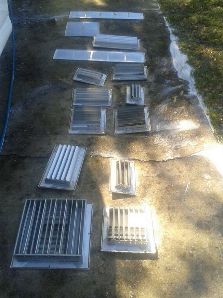 Assorted metal vents and grates laid out on a concrete driveway in sunlight