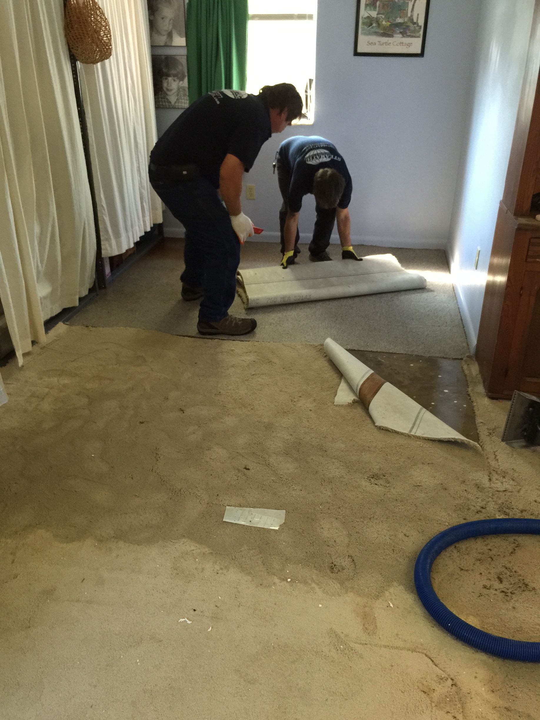 Two people installing flooring in a room, one kneeling while another stands nearby, 