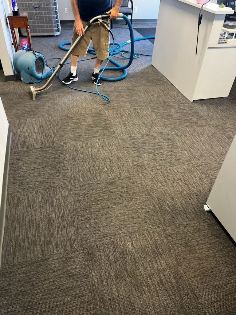 Technician cleaning a carpeted office floor with a vacuum and hose system