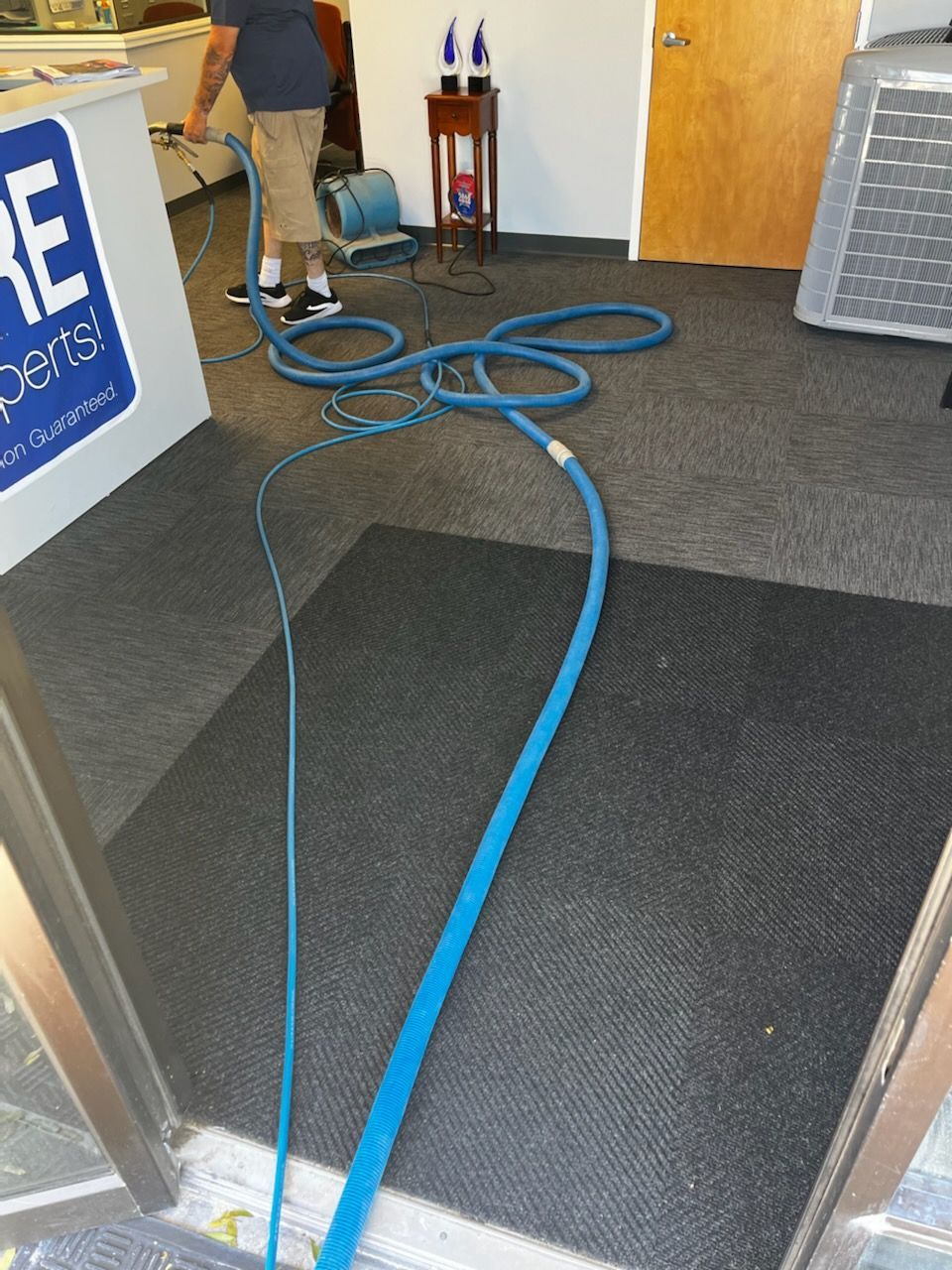 Blue hoses on a carpeted floor in a storefront entrance, with an air machine on the right and cleaning gear in back