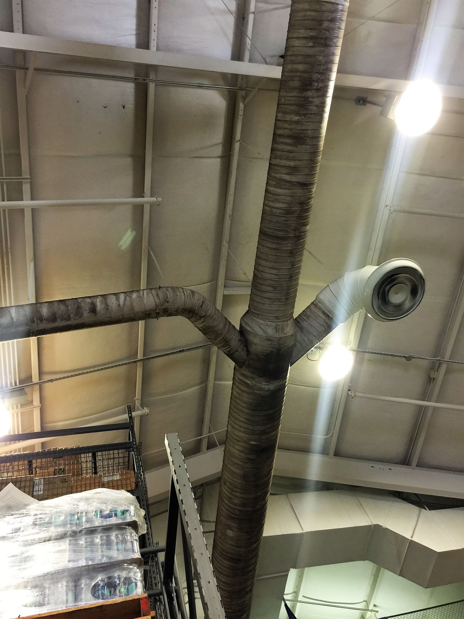 Warehouse ceiling with exposed ductwork, beams, and bright hanging lights