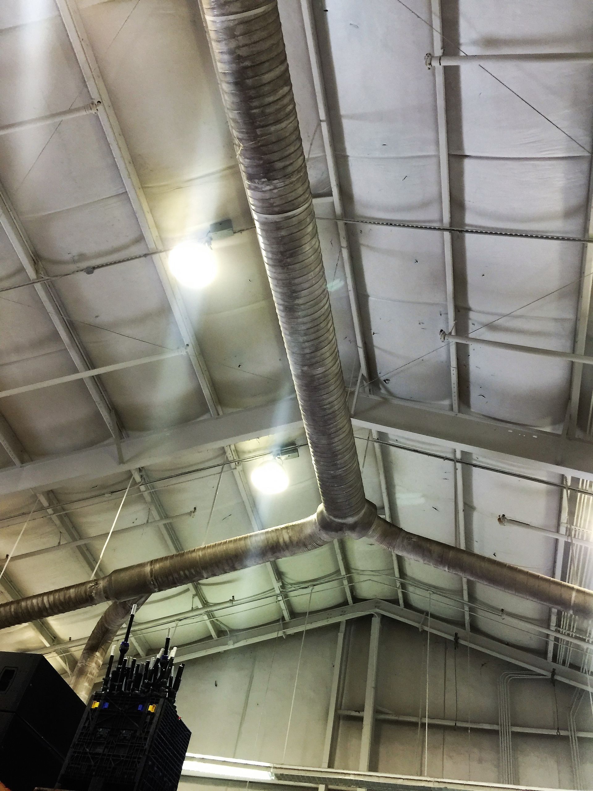 Industrial warehouse ceiling with exposed ducts, white metal panels, and bright overhead lights