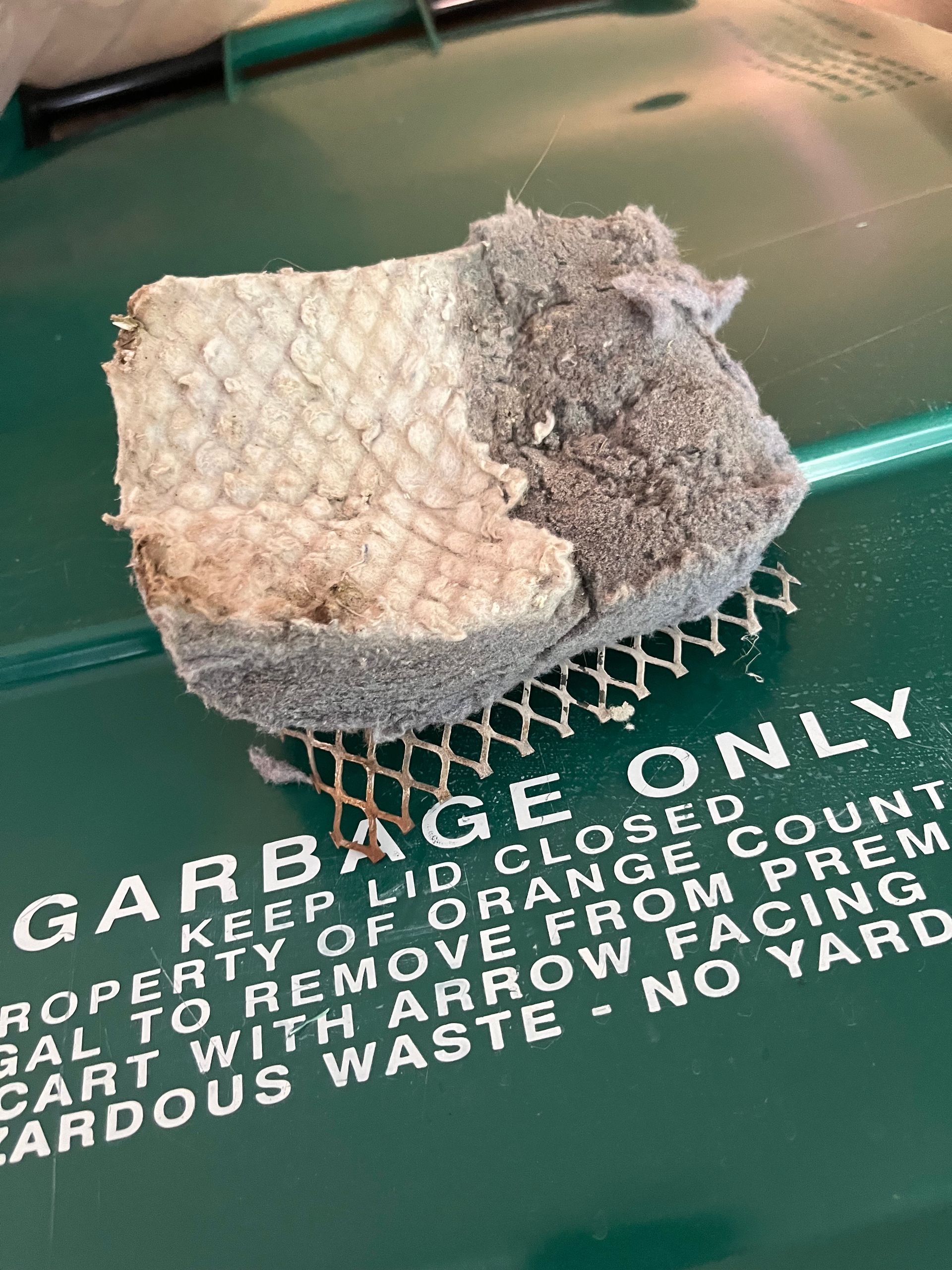 Small dirty white cloth or sponge on a green trash bin labeled “GARBAGE ONLY”