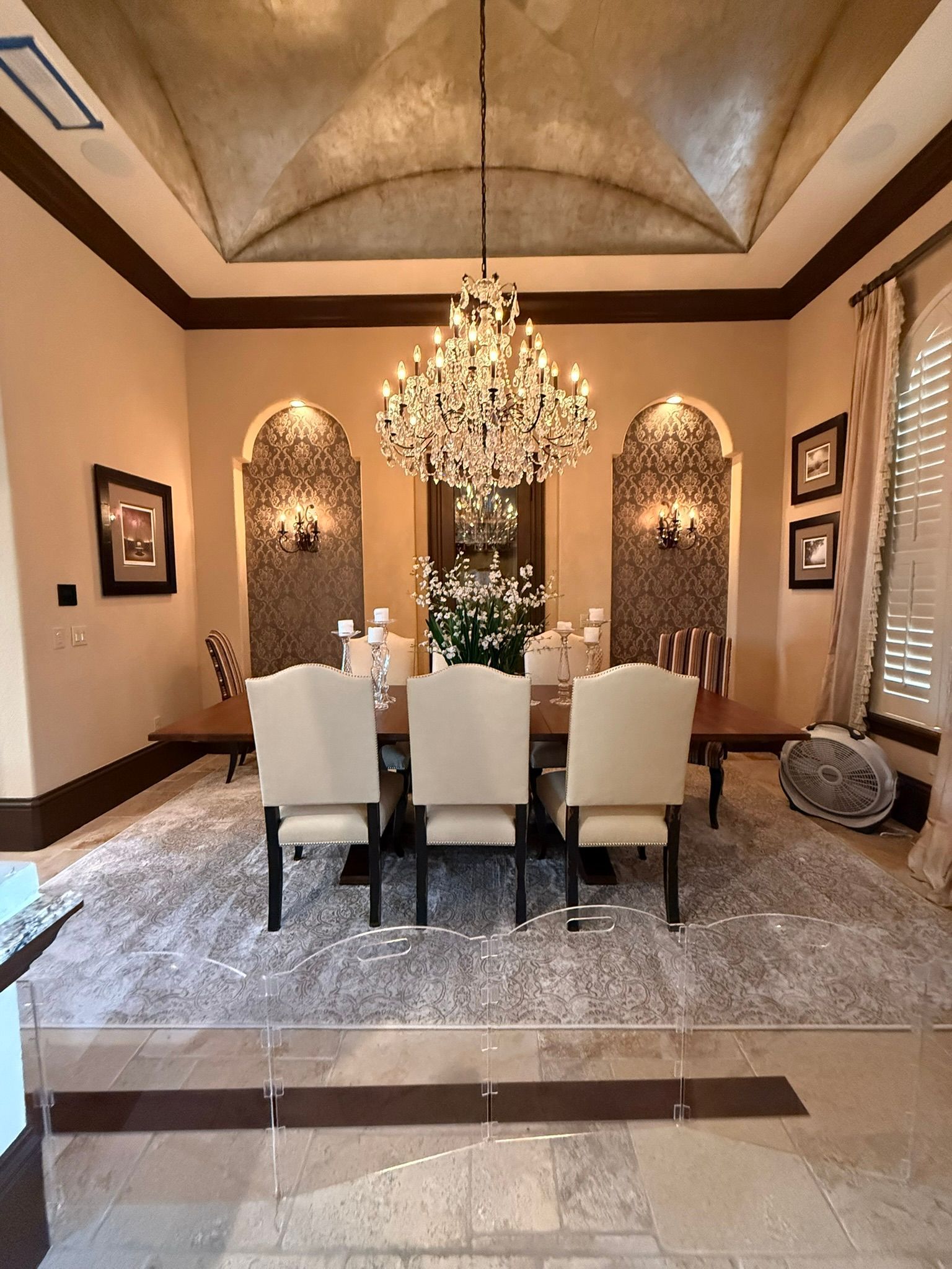 Elegant dining room with chandelier, six cream chairs, and warm tan walls with recessed alcoves.