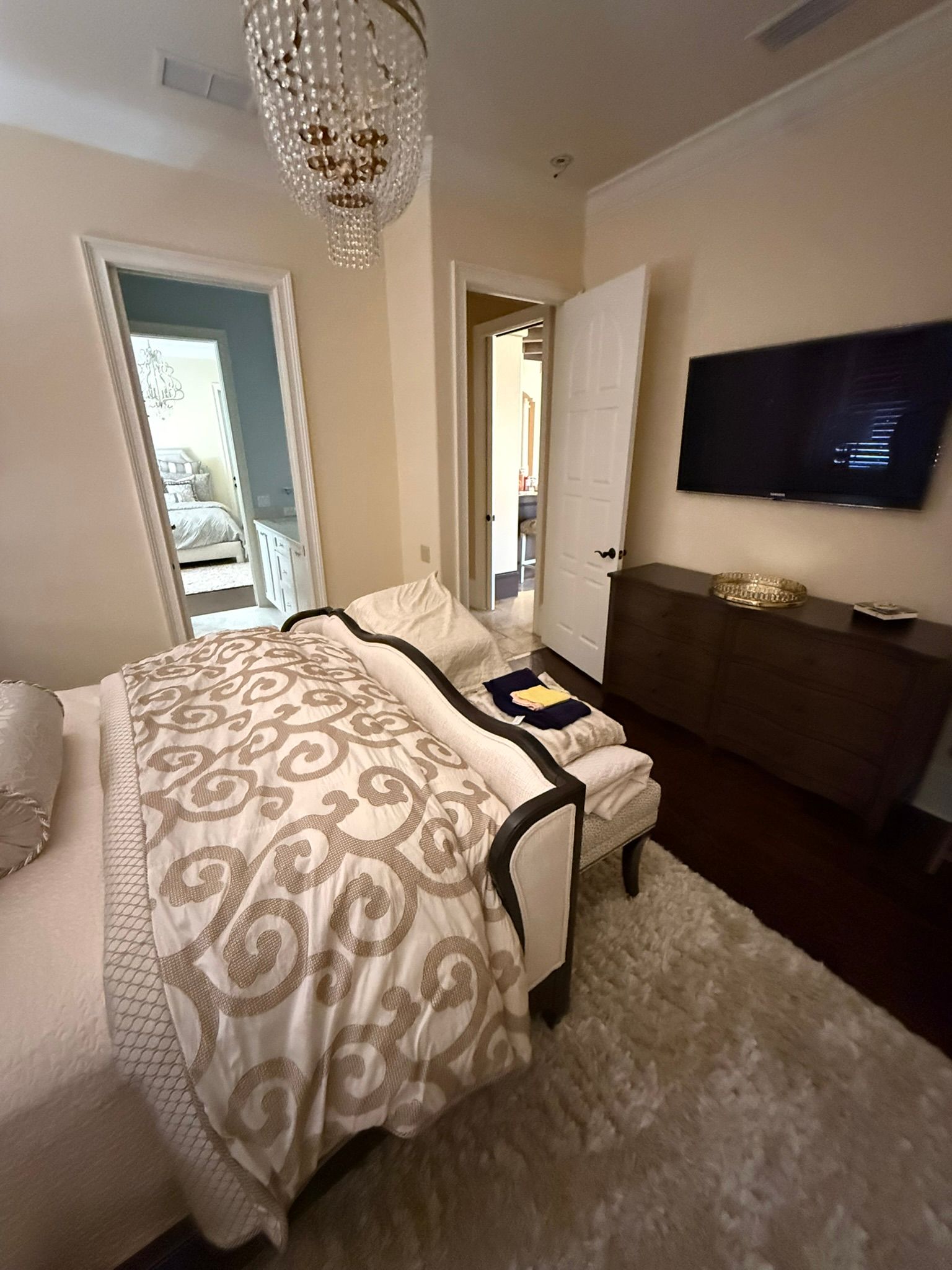 Elegant bedroom with patterned bedspread, chandelier, wall-mounted TV, and balcony doors.
