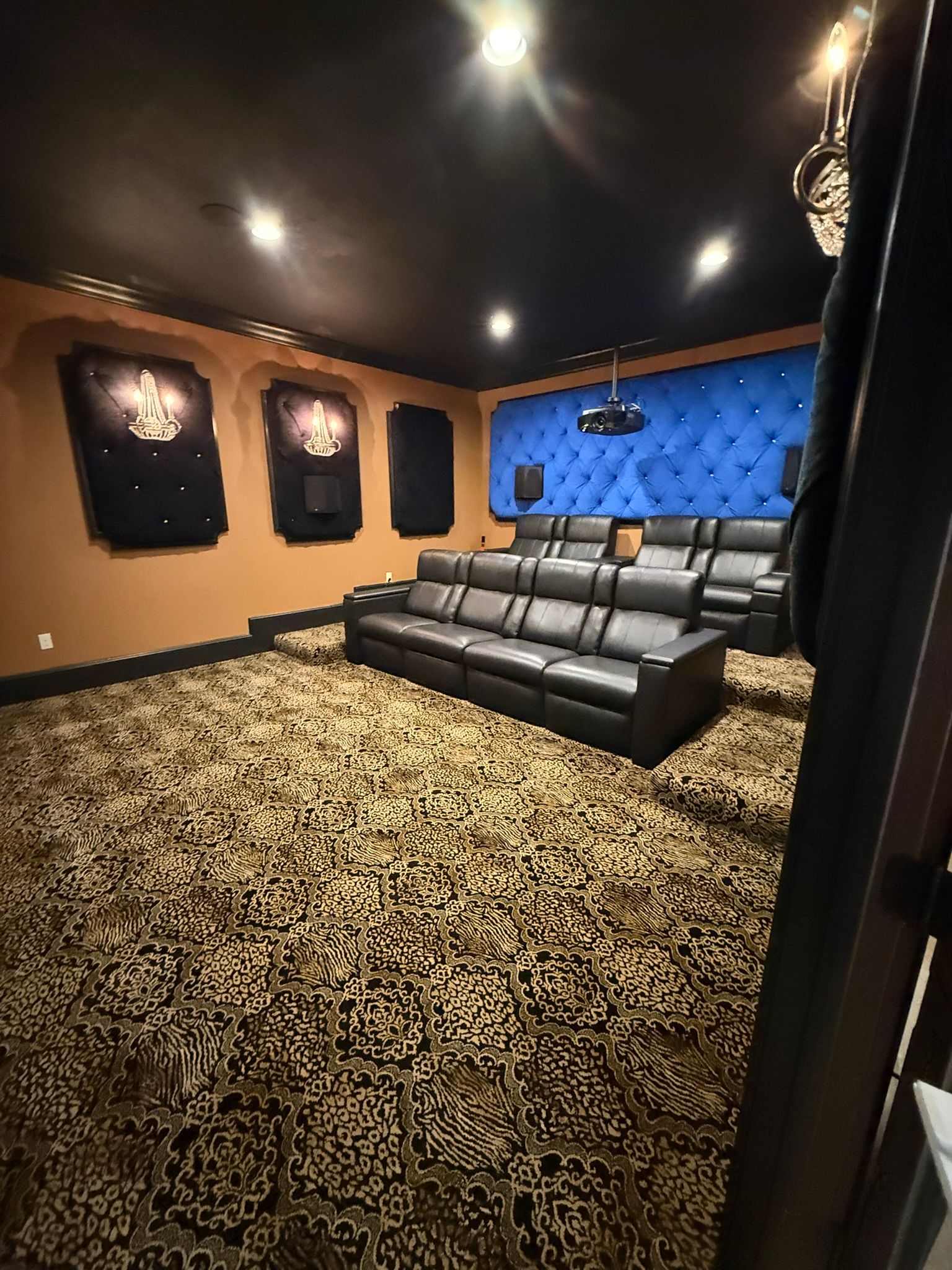 Luxury home theater with black recliners, patterned carpet, blue tufted wall, and recessed ceiling lights