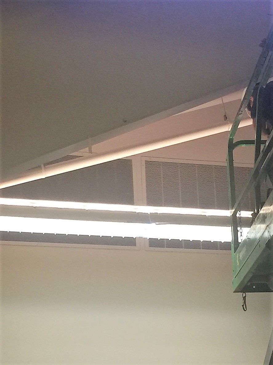 Indoor ceiling corner with exposed beam and fluorescent light fixture beside a metal shelf.