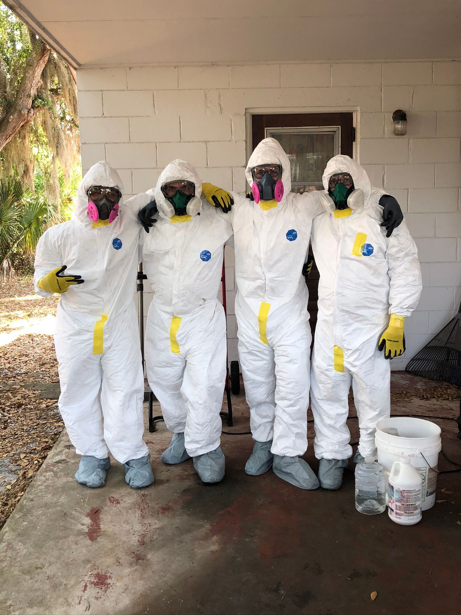 Five people in white hazmat suits and respirators standing outside a house
