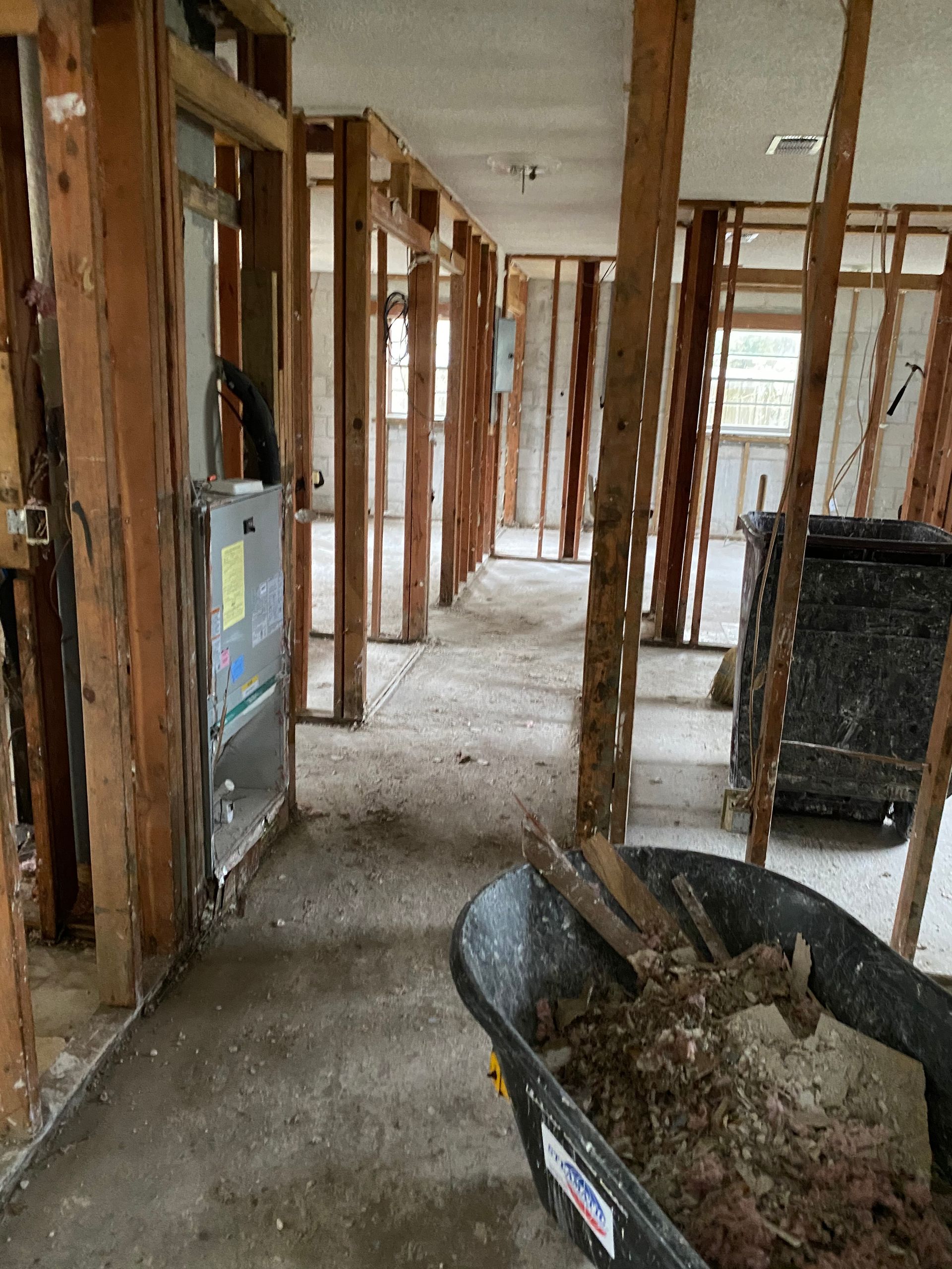 Interior under renovation with exposed studs, debris, and a wheelbarrow in a hallway