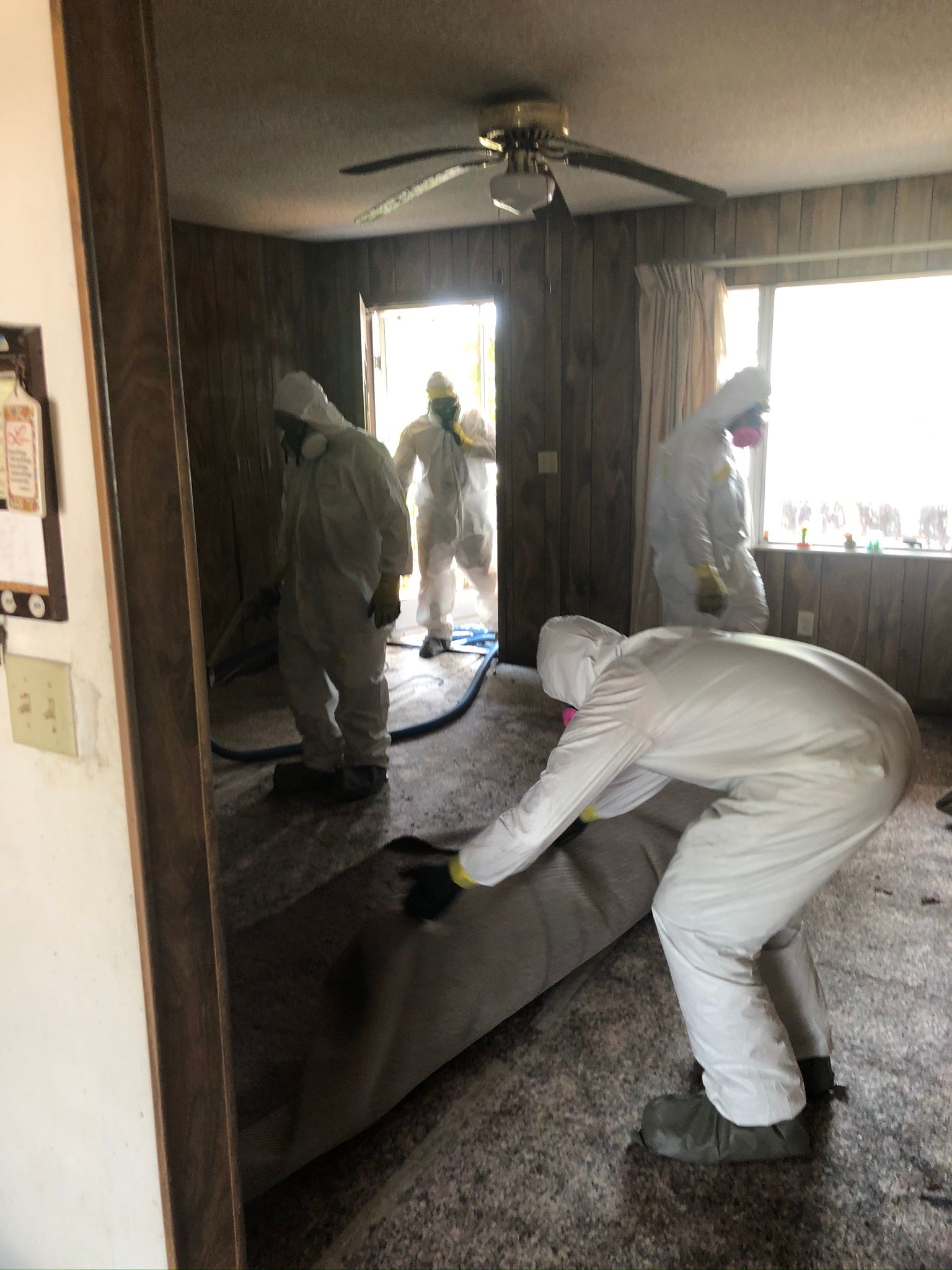 Workers in white protective suits cleaning a living room with a couch and fan.