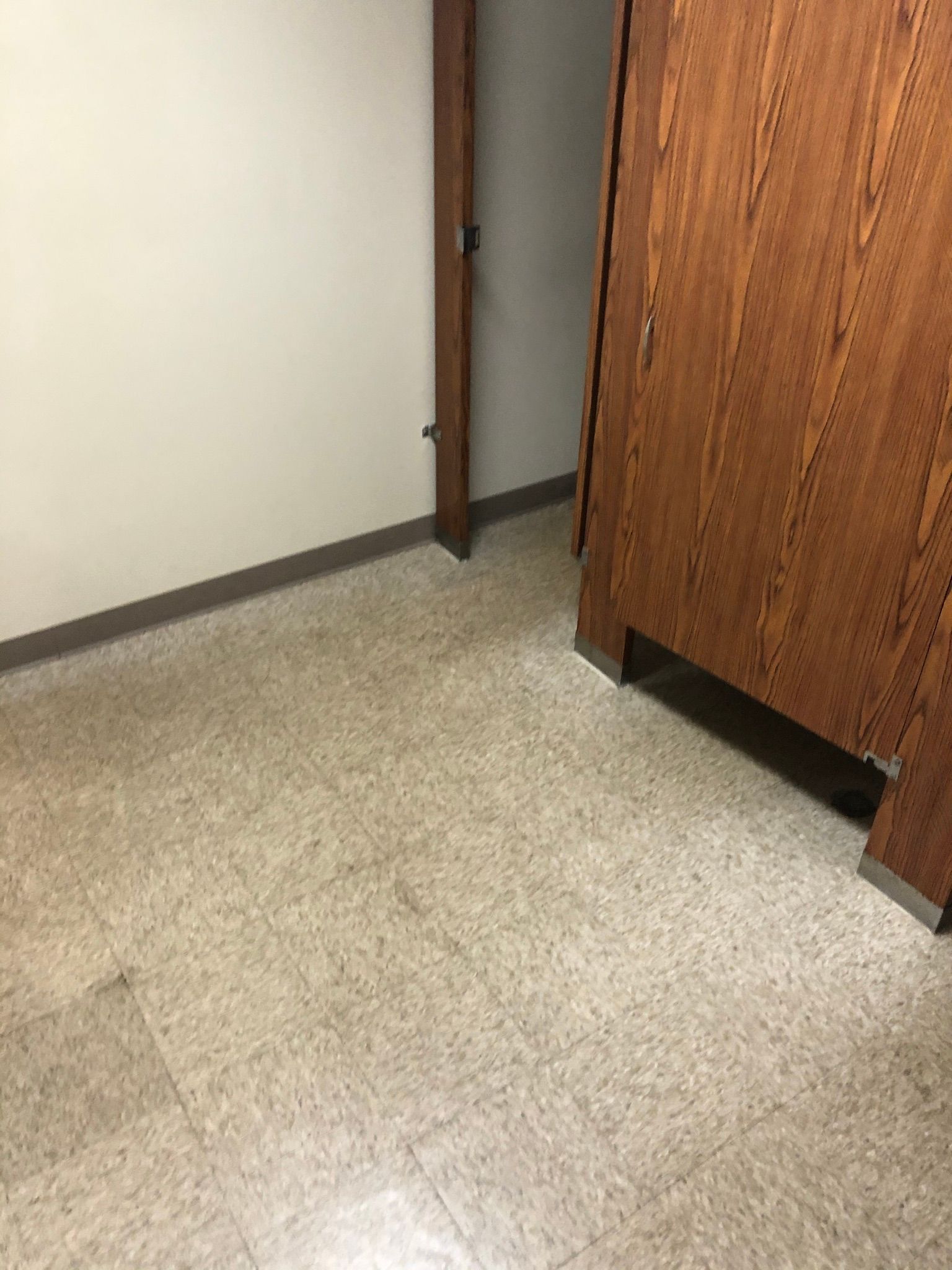 Empty carpeted room corner with beige walls and a wooden cabinet partly blocking the doorway.