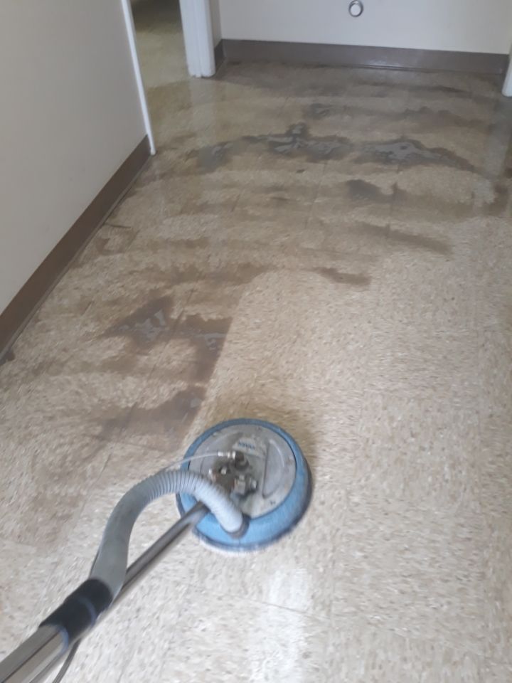 Carpet cleaner vacuuming a stained beige carpet in a hallway