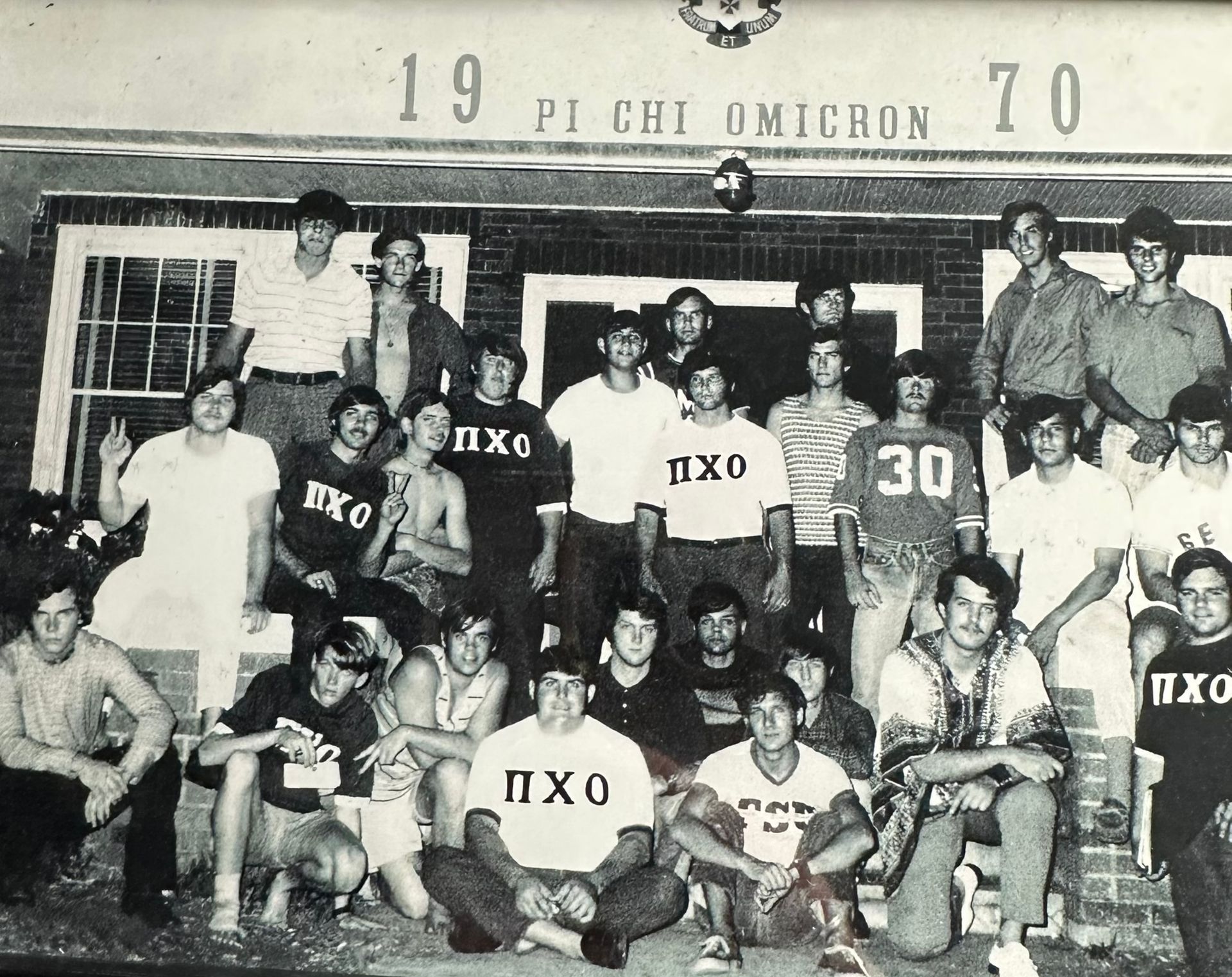 Black-and-white group photo of Pi Kappa Phi members posing in front of a house in 1970.