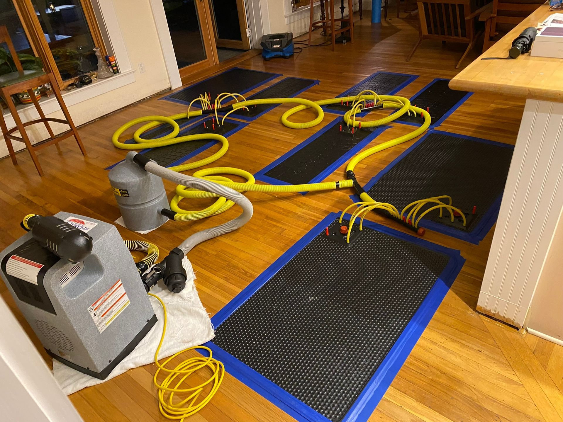 Wooden floor with blue mats and yellow hoses connected to cleaning equipment in a room