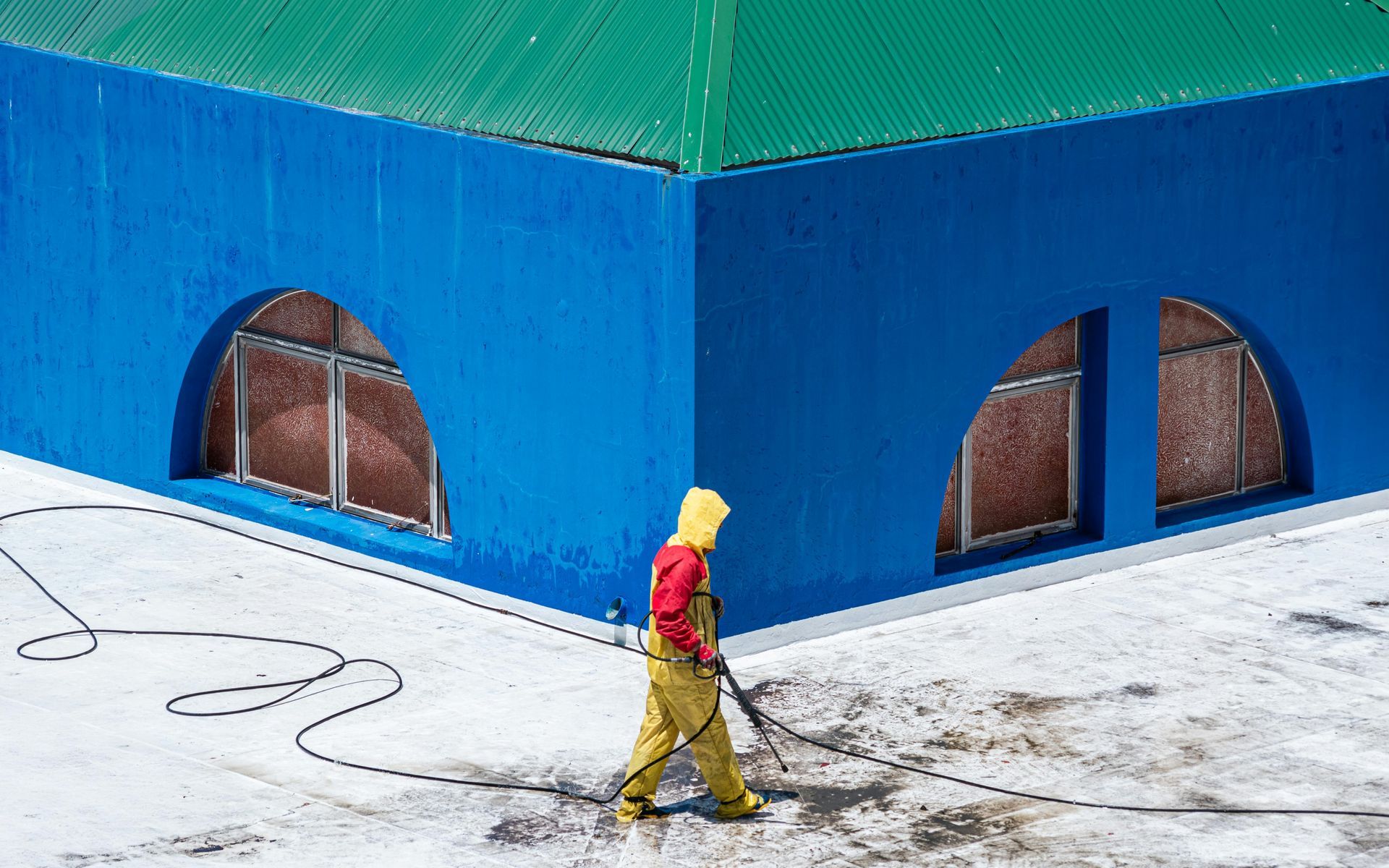 Person in yellow and red walks past a blue building with arched windows on a snowy street.