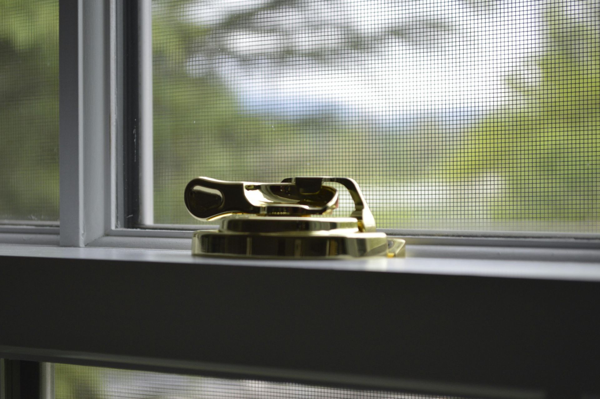 Gold doorstop on a windowsill with a screened window and blurred greenery outside