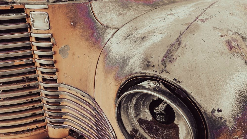 Rusty vintage car front with weathered grille and headlight close-up