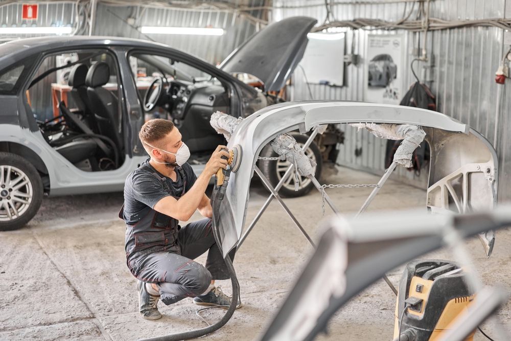 An auto paint technician using a grinding tool to prepare a classic car for painting.