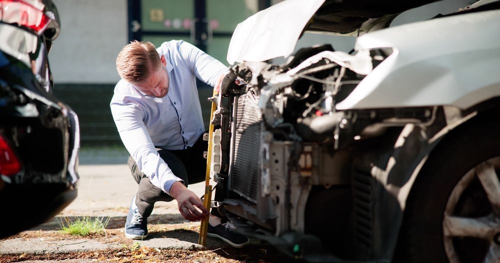 Mechanic inspecting damage on a white car after a collision, with another damaged vehicle nearby