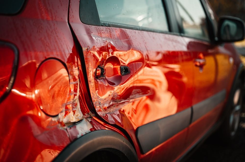 A close up of a red car with a damaged door.