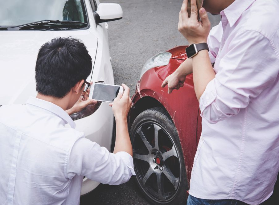 Drivers documenting car accident damage with smartphone before contacting insurance and collision repair